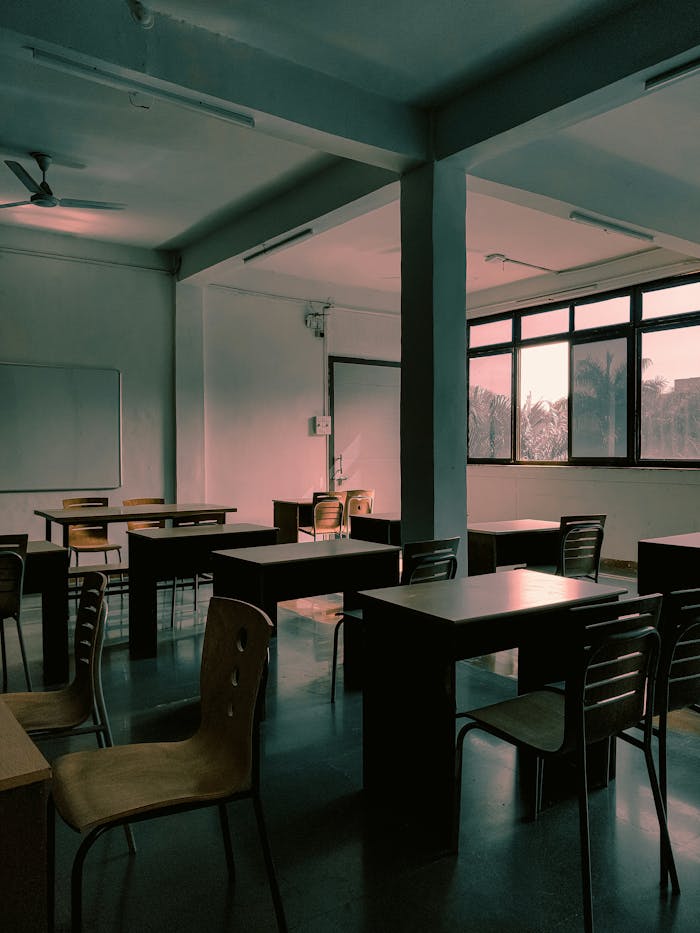 Home Empty classroom with wooden desks and chairs, India, natural sunlight pouring through windows.
