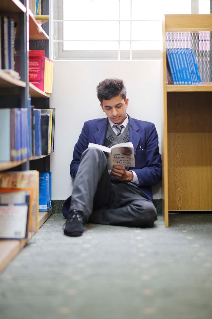 A young student in a school uniform reads a book in a library corner.